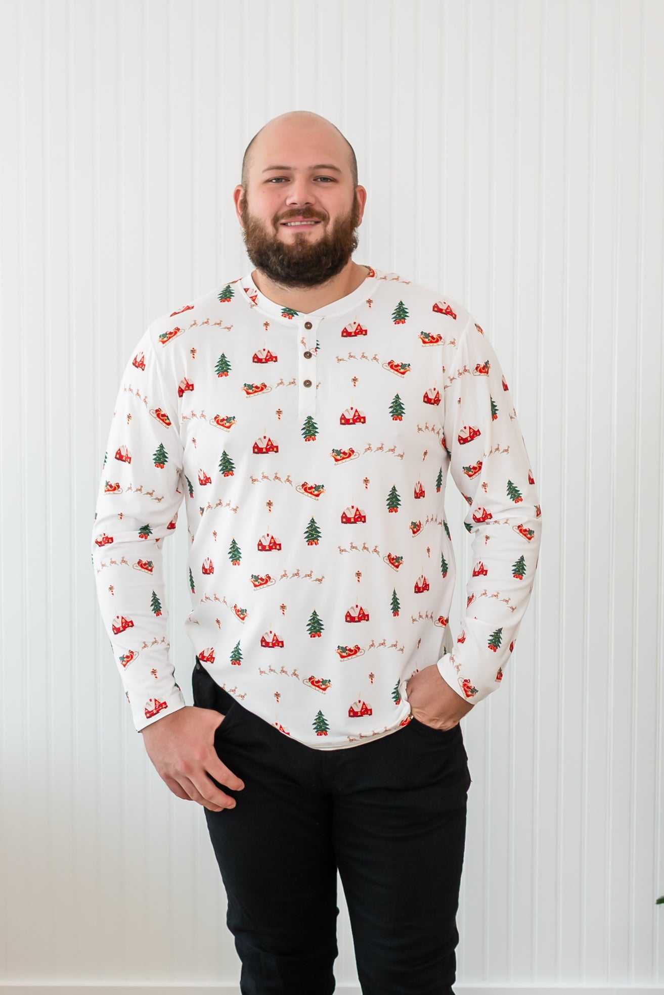 Smiling model wearing the Kyte Men's Long Sleeve Henley Top in Santa Sleigh paired with black jeans