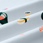 A close-up of a light blue-gray fabric with a repeating sushi print, including nigiri, maki, and sashimi motifs in yellow, green, orange, and white.---1615 1