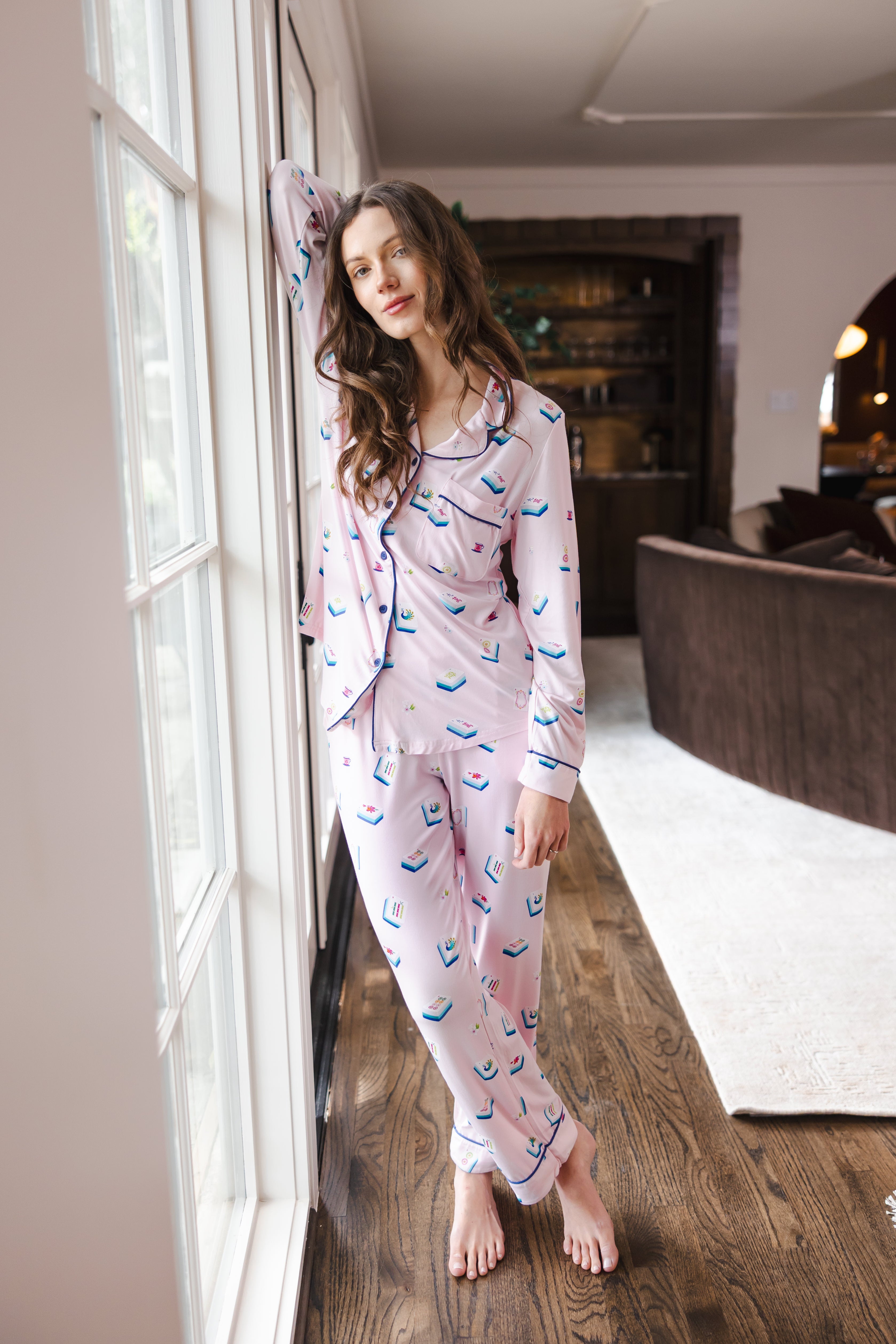 Modal wearing Long-Sleeved Women's Pajama Set in Sakura Mahjong print standing against a window in a living room

