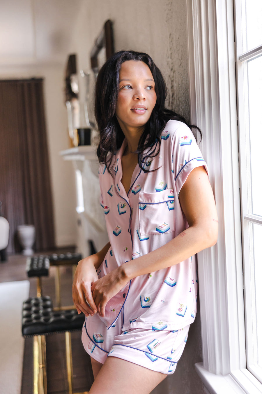 woman wearing pink short sleeve pajama set with mahjong tile print standing against a wall in a living room
