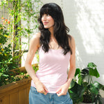 Woman wearing a pink tank top and blue jeans standing outdoors with plants in the background