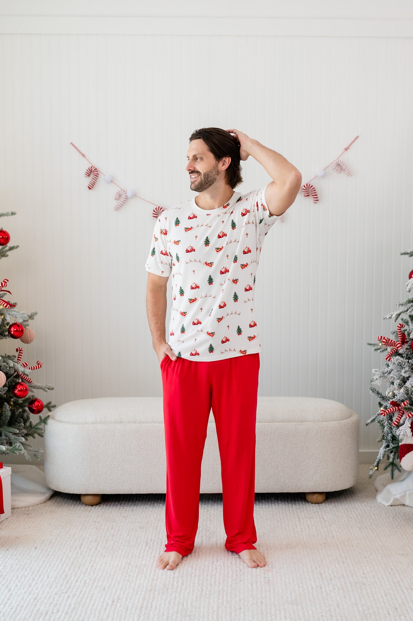 Model wearing the Men's Crew Neck Tee in Santa Sleigh with one arm on his head and Lounge Pants in Cardinal