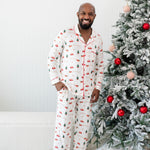 Male model next to a Christmas tree wearing the Kyte Men's Long Sleeve Pajama Set in Santa Sleigh