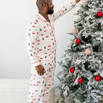 Male model putting an ornament on a Christmas tree while wearing the Men's Long Sleeve Pajama Set in Santa Sleigh
