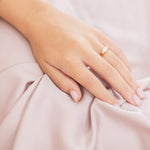 Hand with a ring on a soft pink fabric background