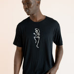 Modal wearing Black Men's Crew Neck Tee with Skeleton print in center over blue jeans on a beige background
