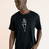 Modal wearing Black Men's Crew Neck Tee with Skeleton print in center over blue jeans on a beige background