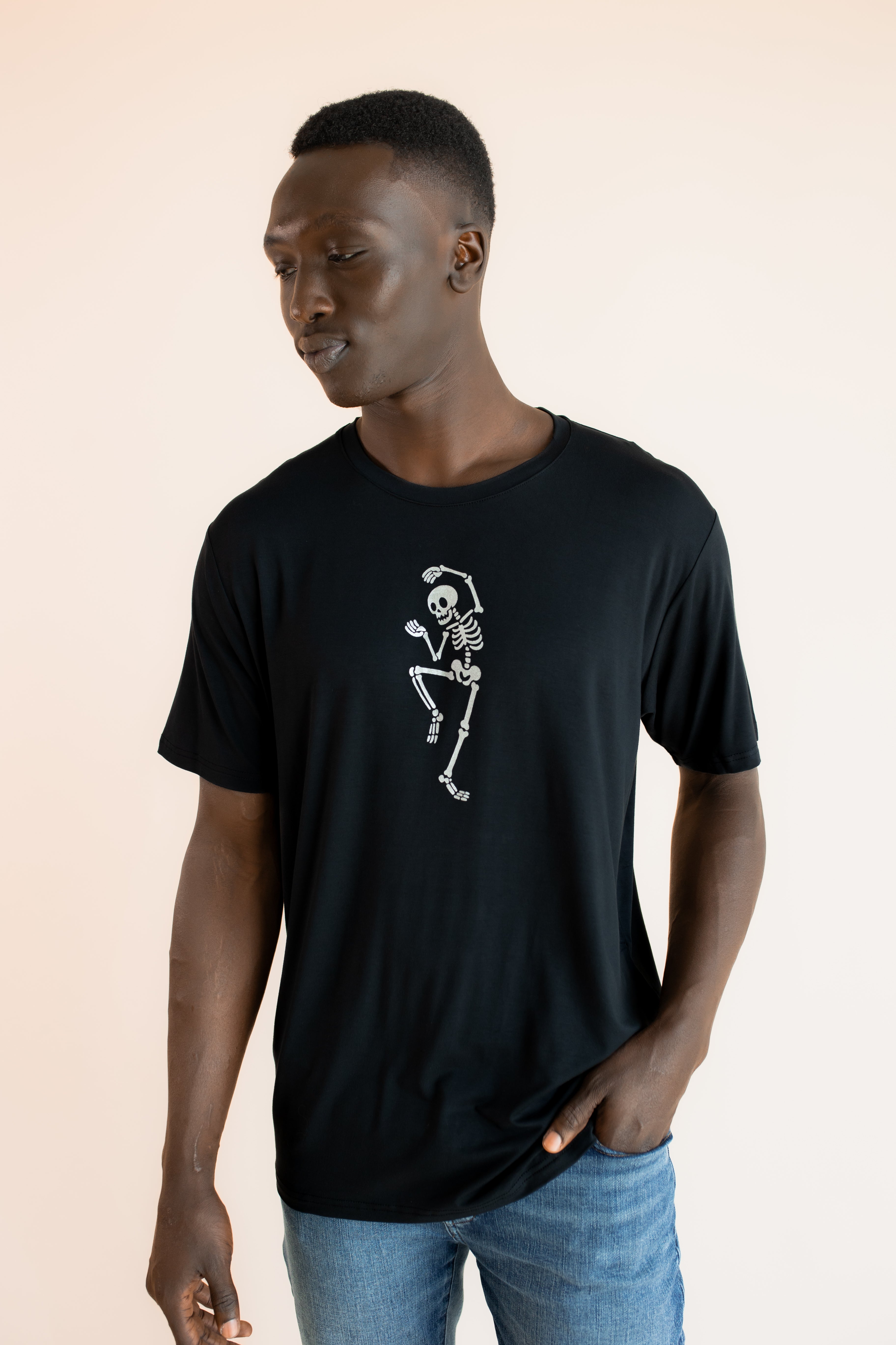 Modal wearing Black Men's Crew Neck Tee with Skeleton print in center over blue jeans on a beige background