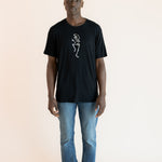 Modal posing in Black Men's Crew Neck Tee with Skeleton print in center over blue jeans on a beige background