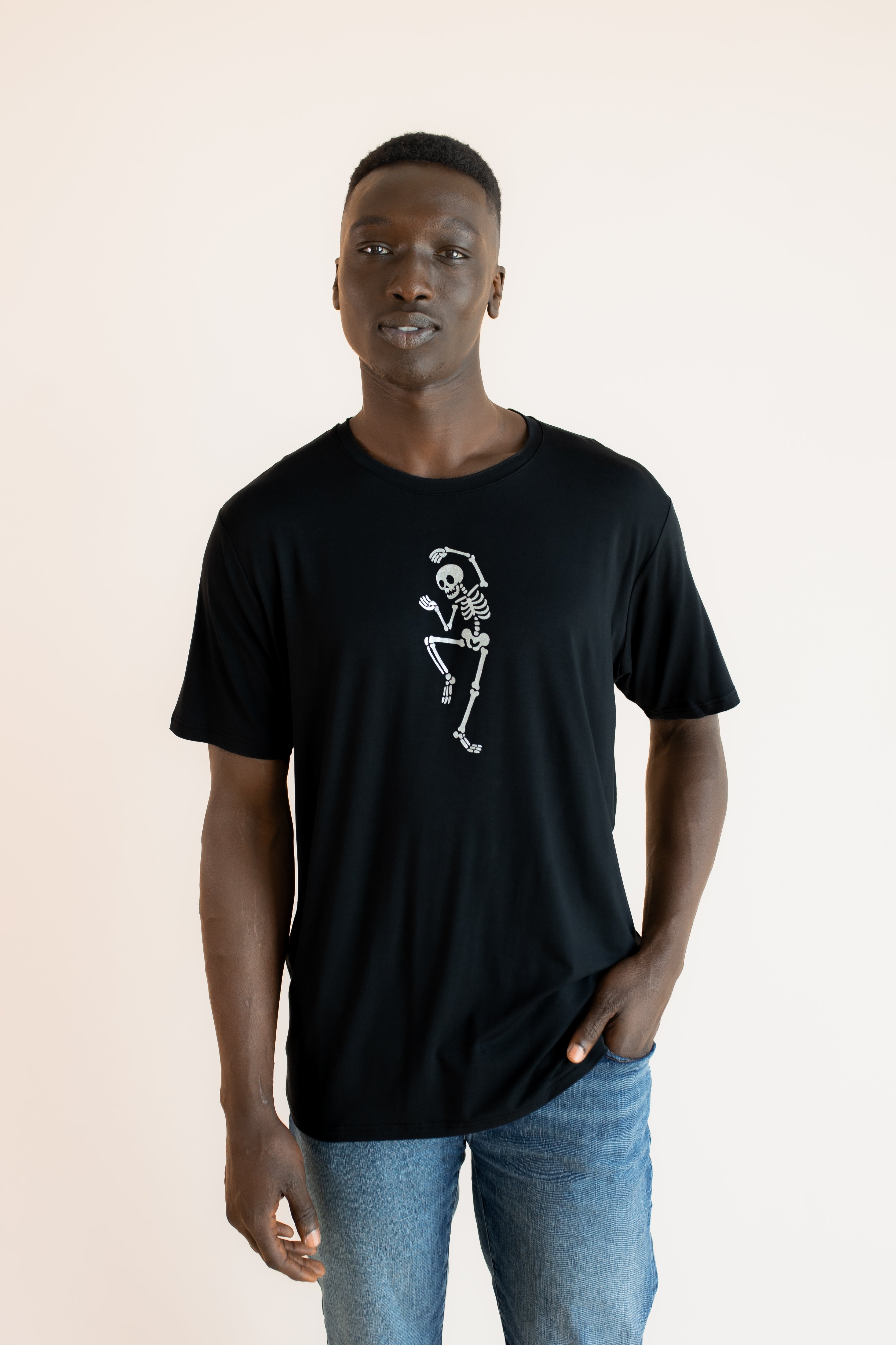 Modal wearing Black Men's Crew Neck Tee with Skeleton print in center over blue jeans on a beige background 