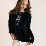 Modal wearing Black Women's Sweatshirt with Skeleton print in the center over white pants on a beige  ::: Model is 5'9.5" wearing size XS ///background