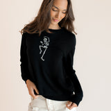 Modal wearing Black Women's Sweatshirt with Skeleton print in the center over white pants on a beige  ::: Model is 5'9.5" wearing size XS ///background