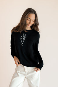 Modal wearing Black Women's Sweatshirt with Skeleton print in the center over white pants on a beige