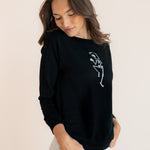 Modal wearing Black Women's Sweatshirt with Skeleton print in the center over white pants on a beige background
