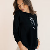 Modal wearing Black Women's Sweatshirt with Skeleton print in the center over white pants on a beige background