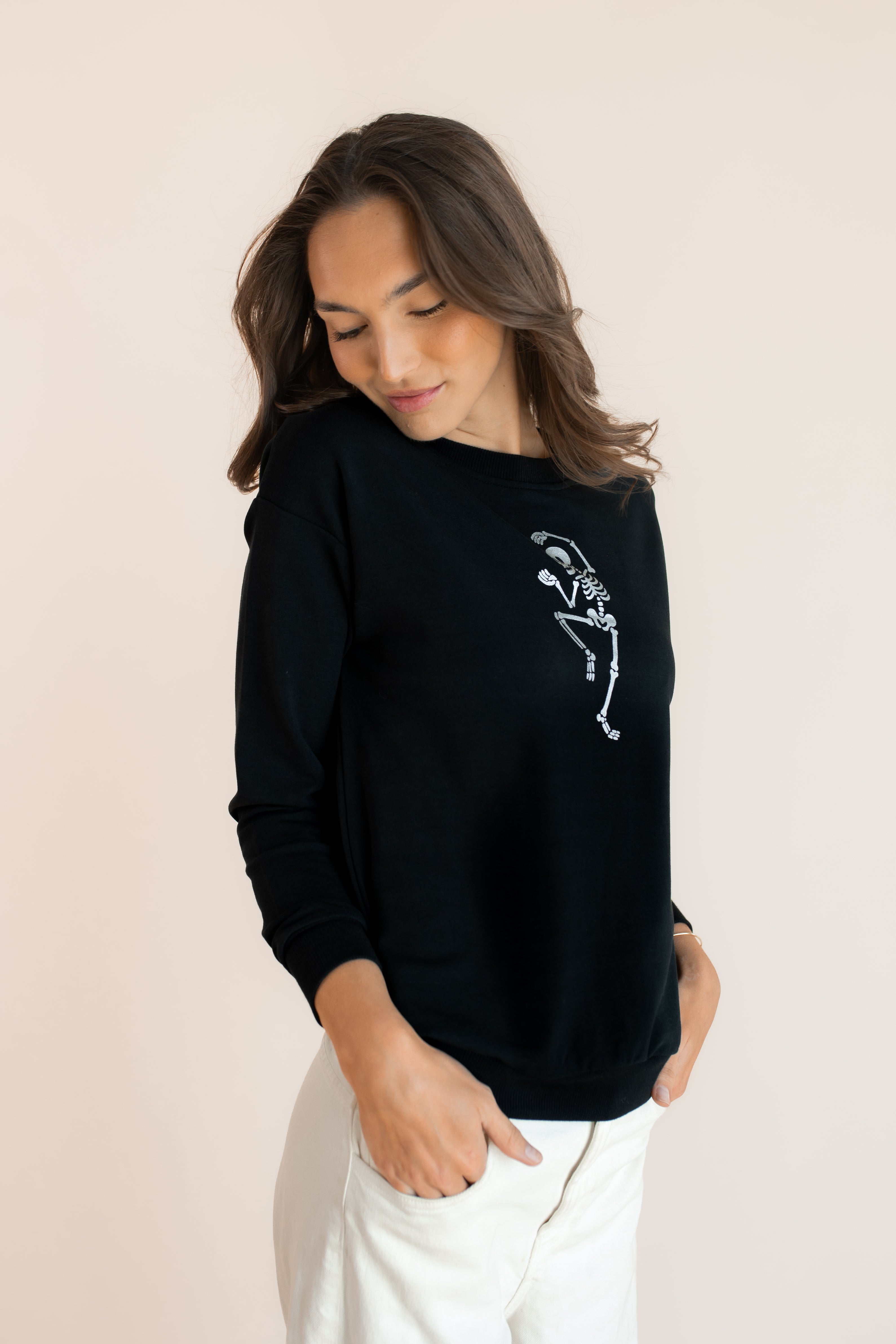 Modal wearing Black Women's Sweatshirt with Skeleton print in the center over white pants on a beige background