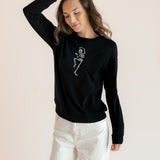 Modal posing in Black Women's Sweatshirt with Skeleton print in the center over white pants on a beige background