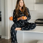 Woman in black skeleton pajamas sitting on a kitchen counter holding small pumpkins.