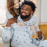 Male sitting on the couch wearing the Men's Long Sleeve Pajama Set in Ski with his wife standing behind him with her arms around her shoulders matching in women's ski pajama set
