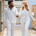 Couple holding hands walking on a tiled sidewalk in front of a house matching in Women's and Men's Long Sleeve Pajama Set in Ski