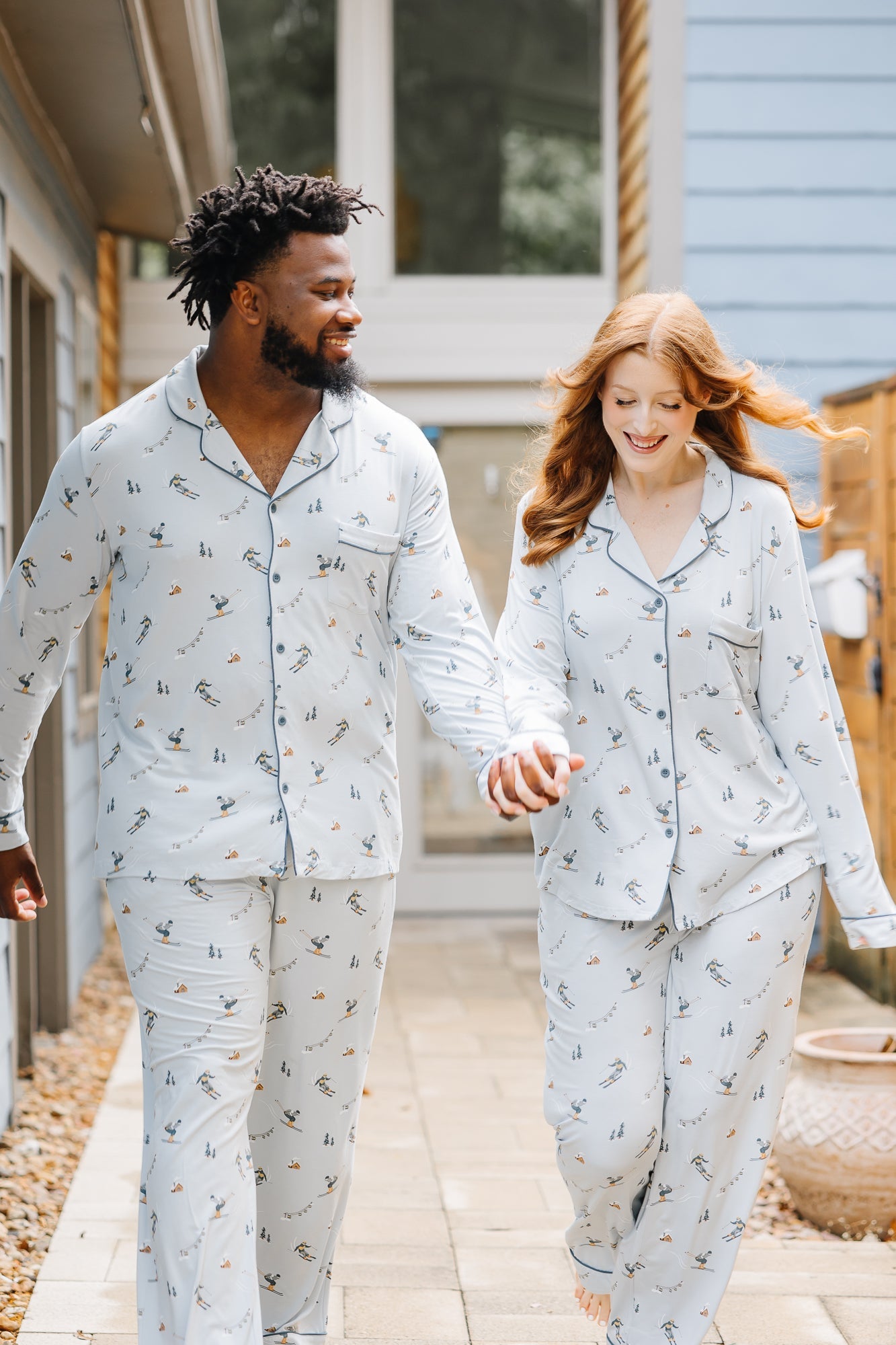 Smiling couple walking down a sidewalk wearing matching Men's and Long-Sleeved Women's Pajama Set in Ski