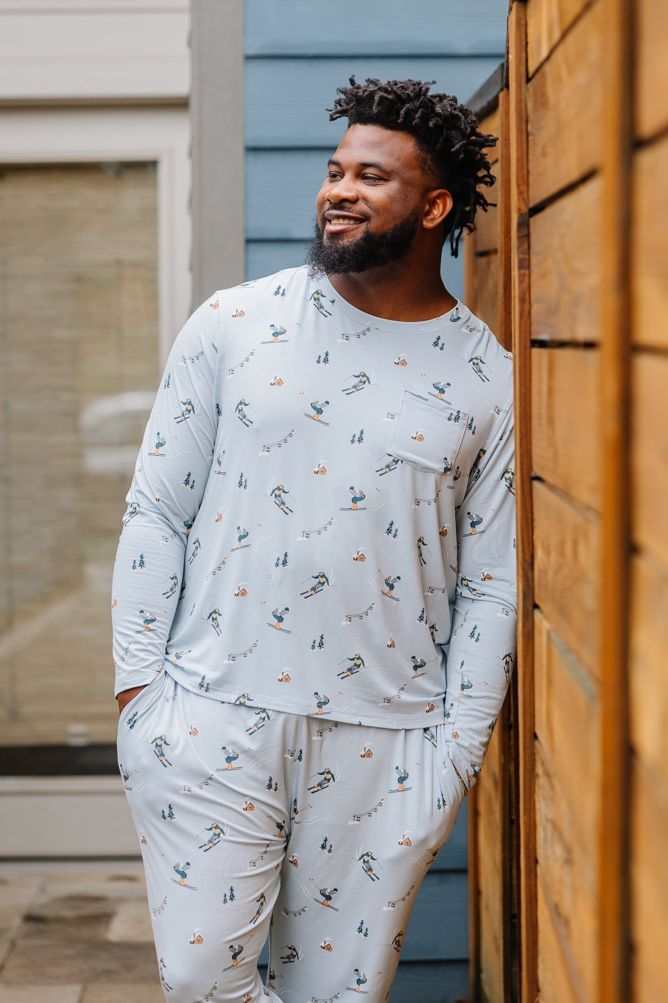 Smiling male model wearing the Men's Jogger Set in Ski looking off to the side leaning up against a fence 