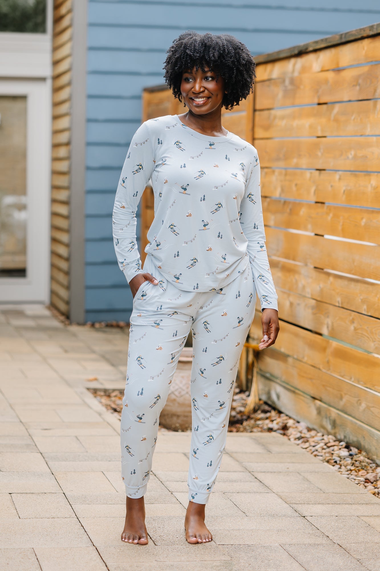 Smiling model standing beside a wooden fence wearing the Women's Jogger Pajama Set in Ski
