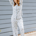 Female model standing outside beside a blue paneled house wearing the Long-Sleeved Women's Pajama Set in Ski with her arms stacked on top of her head