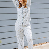 Female model standing outside beside a blue paneled house wearing the Long-Sleeved Women's Pajama Set in Ski with her arms stacked on top of her head