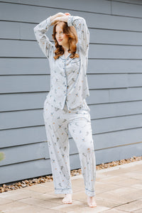 Female model standing outside beside a blue paneled house wearing the Long-Sleeved Women's Pajama Set in Ski with her arms stacked on top of her head  ::: Model is 5'7" wearing size M ///