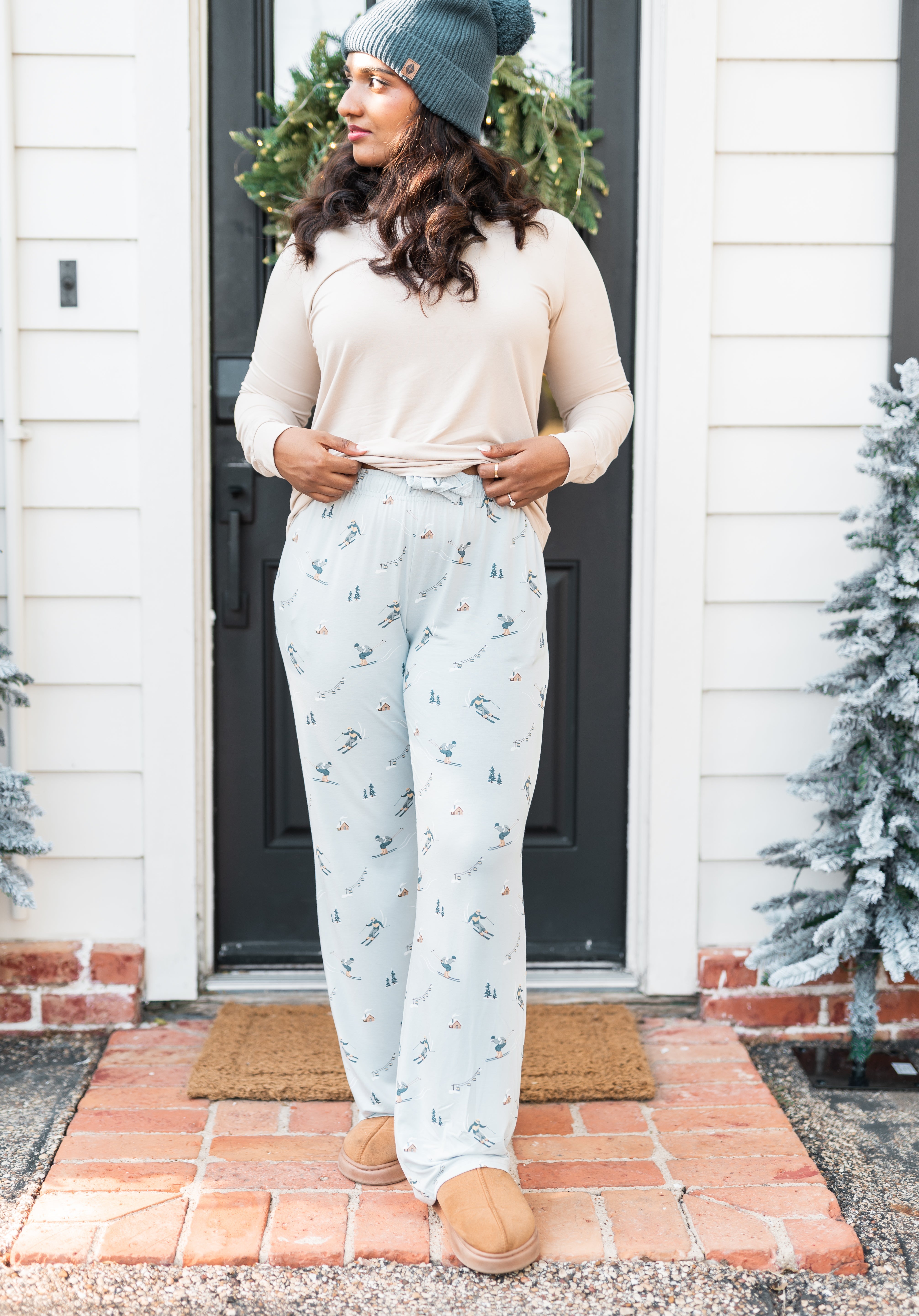 Female standing at a front door wearing the Women's Lounge Pants in Ski with a cream colored shirt and atlantic beanie