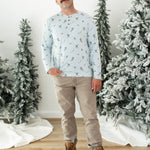 Smiling male modeling the Men's Long Sleeve Henley Top in Ski with khaki colored pants and light brown boots standing between frosted trees