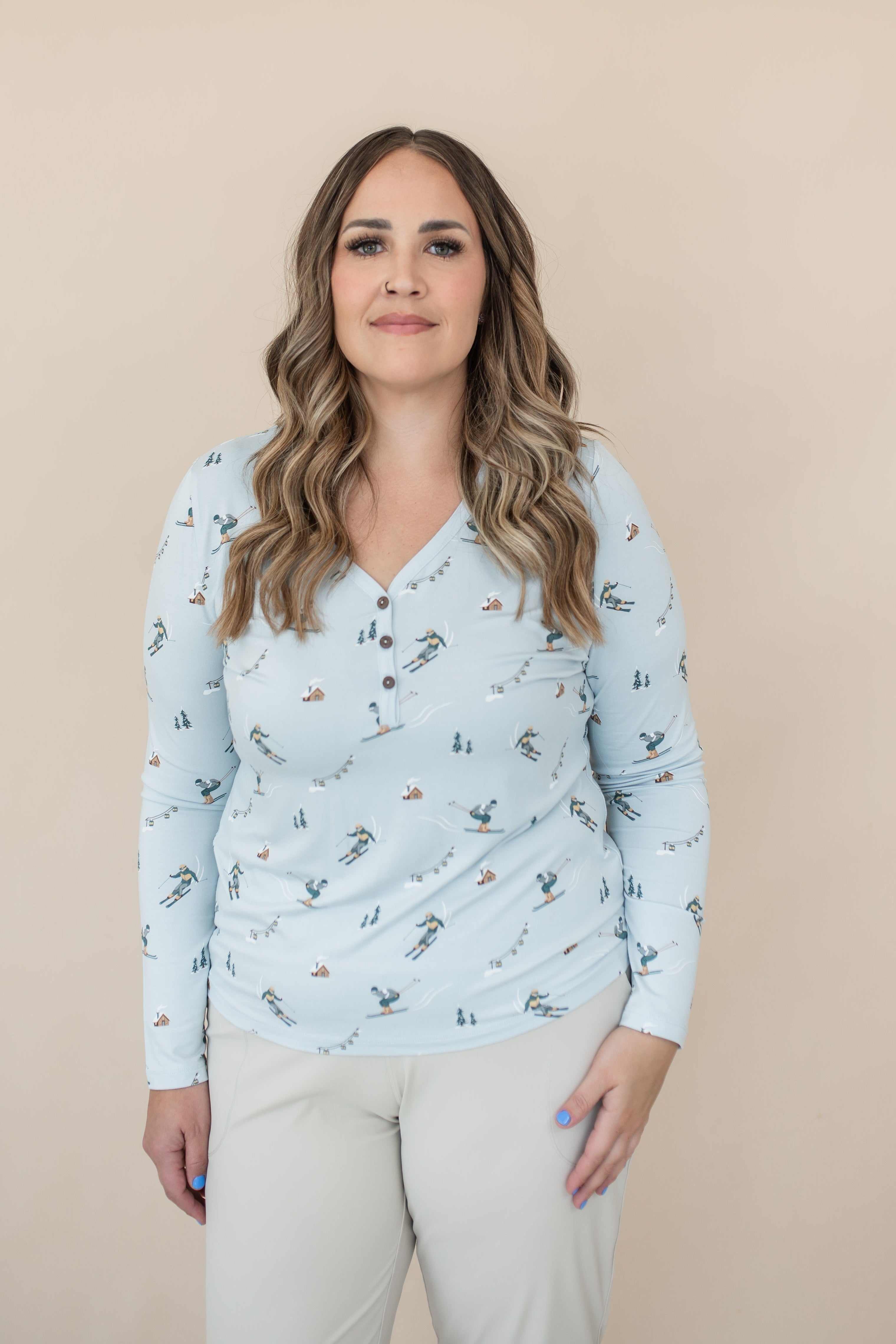 Female model wearing the Women's Long Sleeve Henley Tee in Ski with light beige pants standing in front of a light neutral background