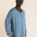 A man wearing a light blue long-sleeve sleep sack, standing against a solid beige background.