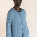 A man wearing a light blue long-sleeve sleep sack, standing against a solid beige background.