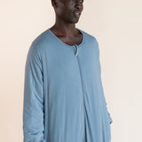 A man wearing a light blue long-sleeve sleep sack, standing against a solid beige background.