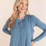 A smiling blonde woman wearing a dusty blue sleeveless-sleeve sleep sack with matching shirt underneath