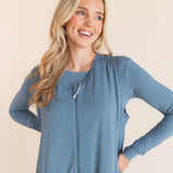A smiling blonde woman wearing a dusty blue sleeveless-sleeve sleep sack with matching shirt underneath