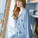 Woman in light blue pajamas sitting on a white surface with a bookshelf in the background.