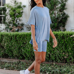 Woman in light blue outfit standing outdoors with greenery in the background