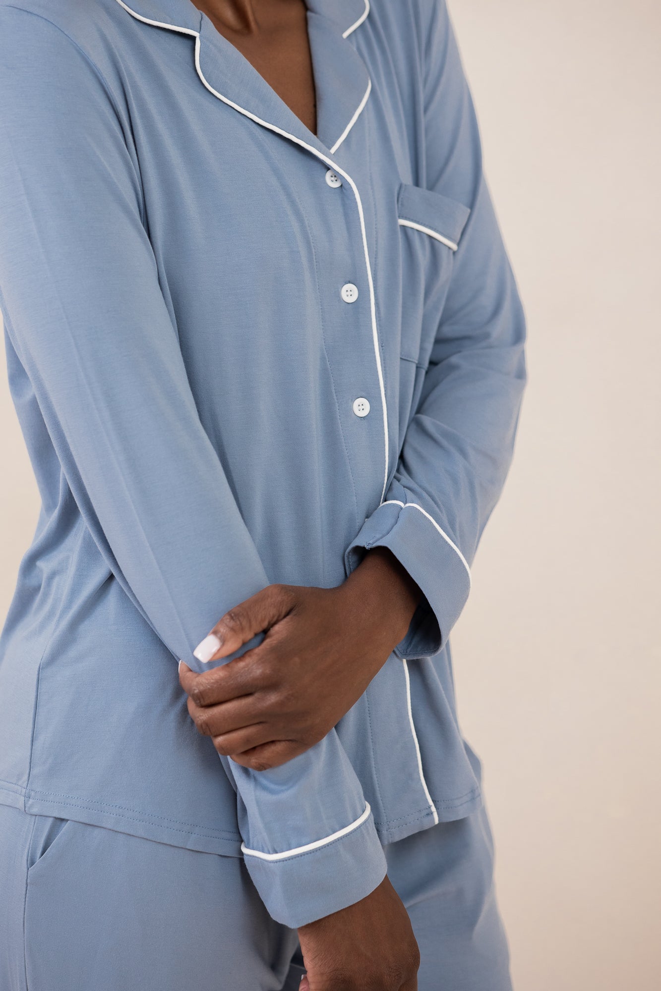 Woman modeling slate blue button up pajamas with white piping against a tan backdrop