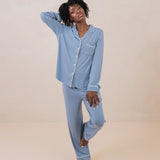Woman modeling slate blue button up pajamas with white piping against a tan backdrop