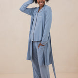 Woman modeling slate blue button up pajamas with white piping against a tan backdrop with matching slate robe