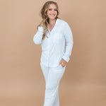 Smiling model standing with one hand bottom's pocket and one hand in her hair while wearing the Long-Sleeved Women's Pajama Set in Small Mist Stripe