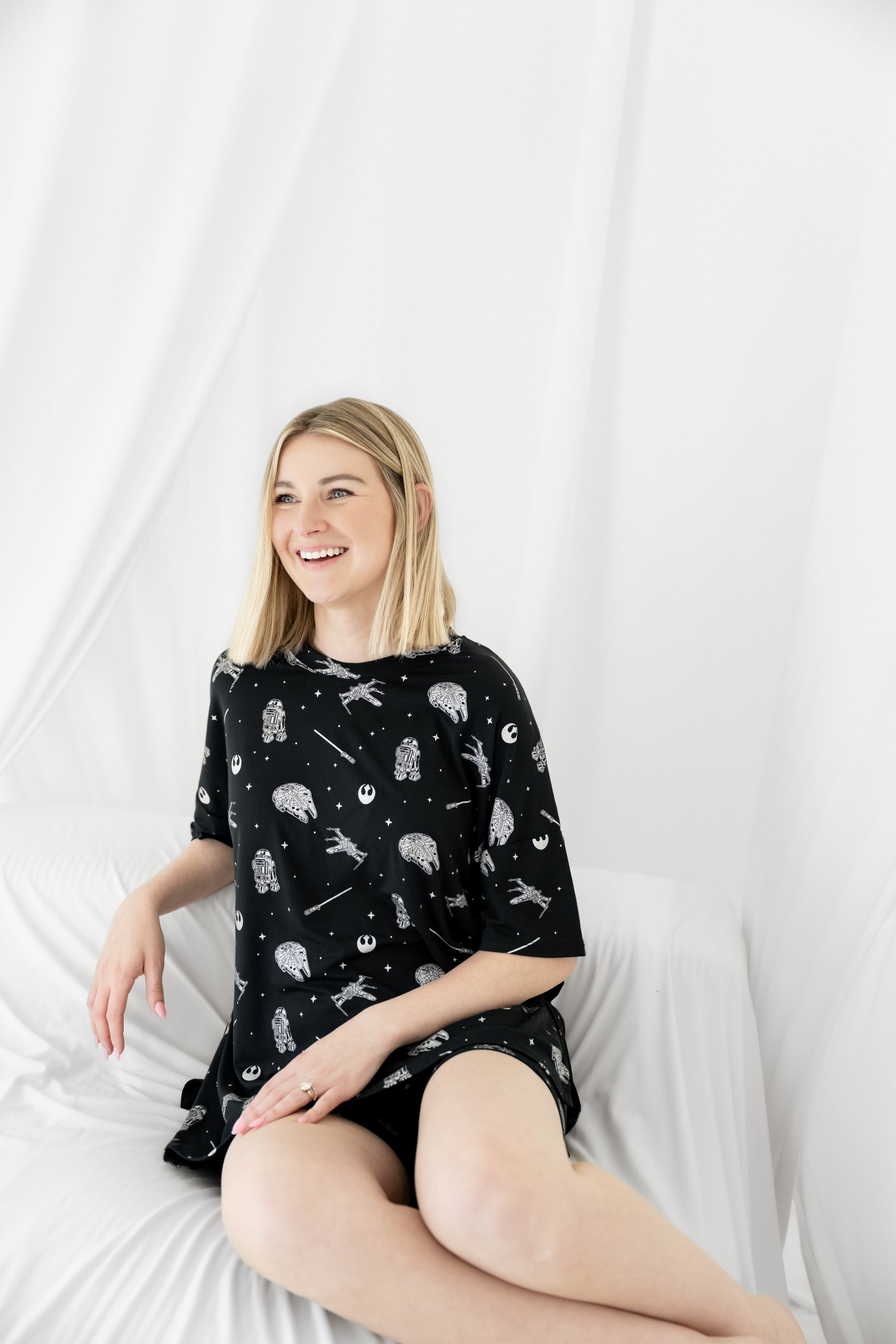 Smiling female sitting in a white blanket wearing the Women’s Biker Short Set in STAR WARS™