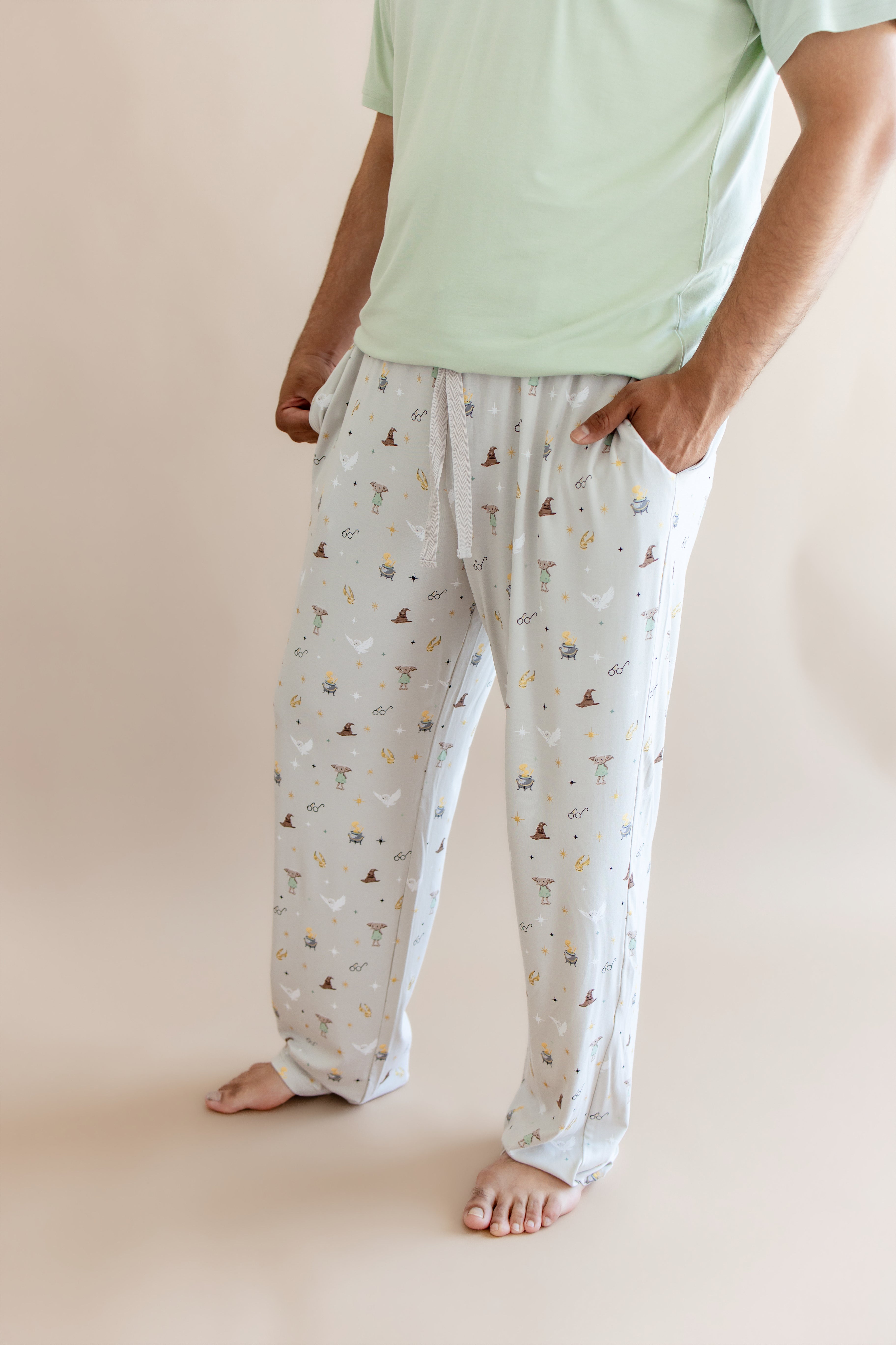 Person wearing cream men's lounge pant with pockets having Harry Potter prints with green shirt on a beige background