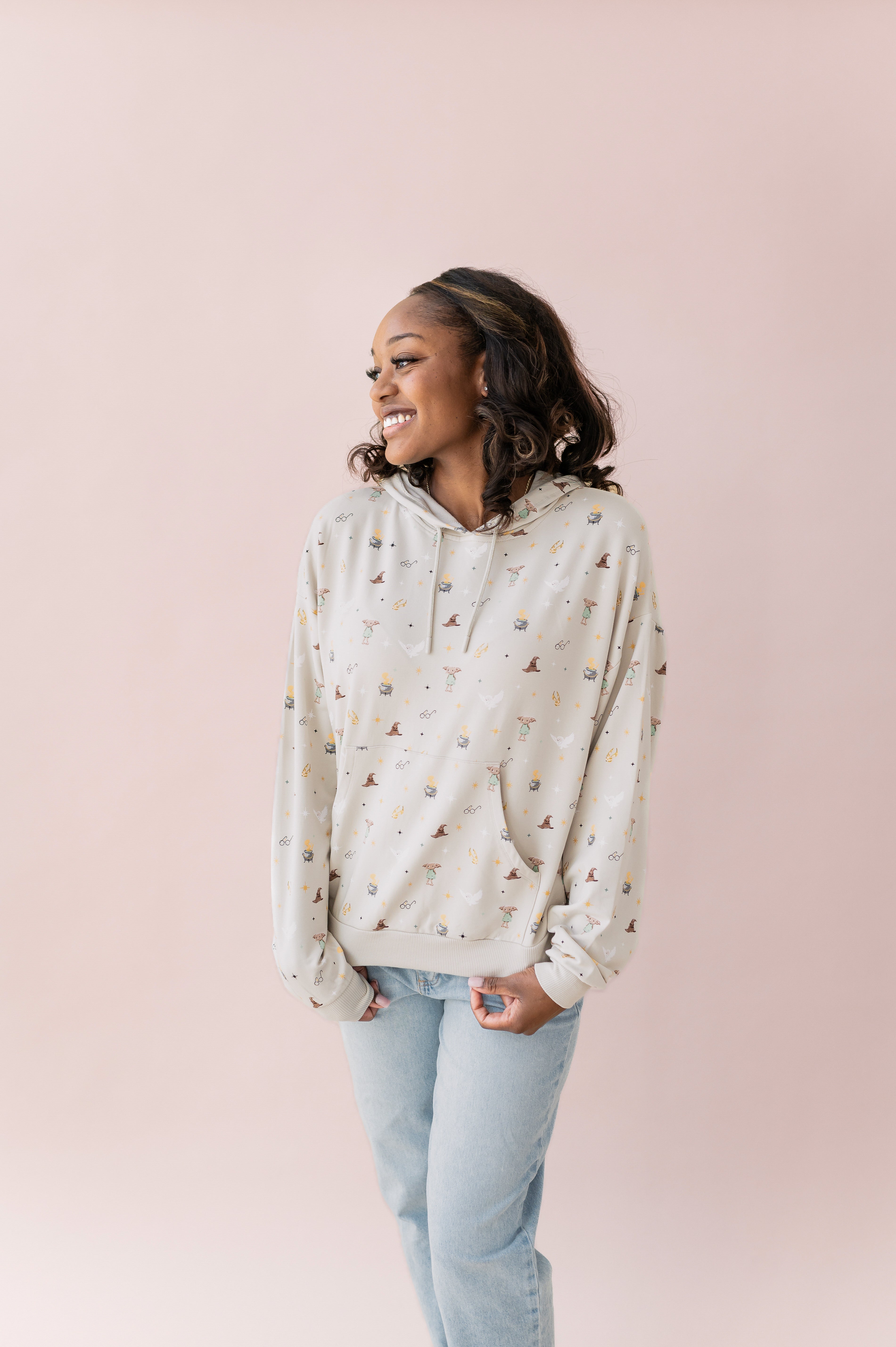 Woman wearing a beige hoodie with Harry Potter icons printed and blue jeans
