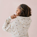 Woman wearing a beige hoodie with Harry Potter icons printed and blue jeans showing off the hood of hoodie