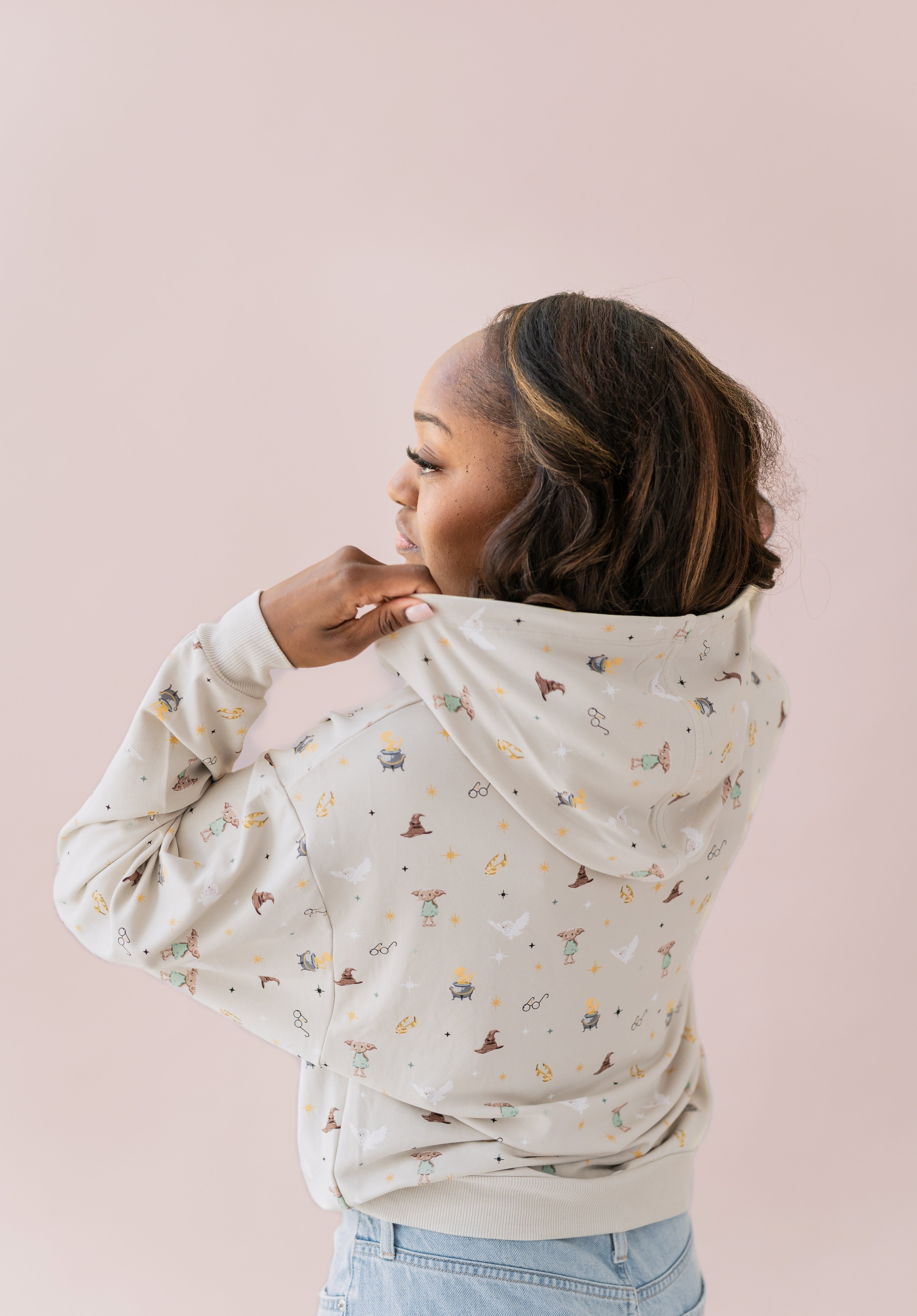 Woman wearing a beige hoodie with Harry Potter icons printed and blue jeans showing off the hood of hoodie