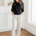 Model standing in a room wearing a cream lounge pant with pockets having Harry Potter prints with a black t-shirt
